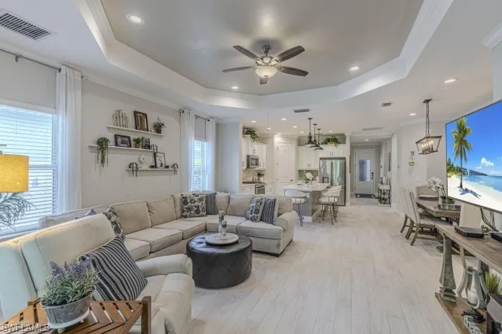 Living room with ceiling fan, light wood-type flooring, crown molding, a tray ceiling, and recessed lighting