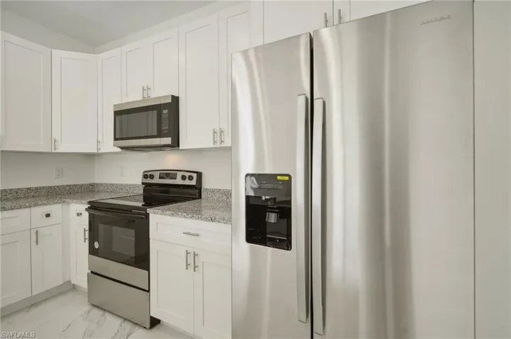 Kitchen with white cabinets, light stone countertops, appliances with stainless steel finishes, and light tile patterned floors