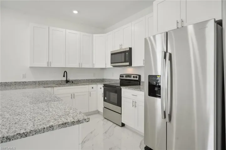 Kitchen with white cabinetry, stainless steel appliances, sink, light stone countertops, and light tile patterned floors