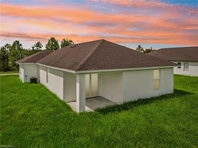 Back house at dusk with a patio, a lawn, and central AC unit