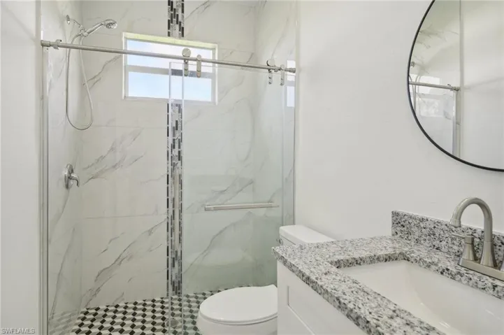 Bathroom featuring a shower with door, toilet, and vanity