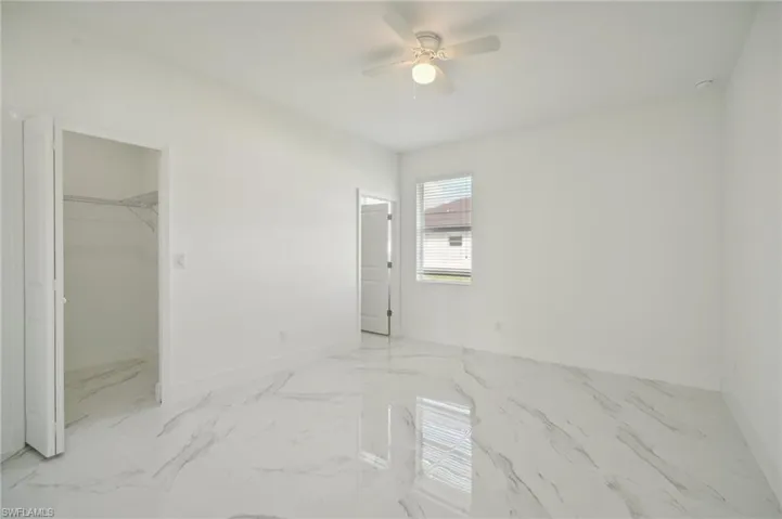 Unfurnished bedroom with a walk in closet, a closet, light tile patterned floors, and ceiling fan