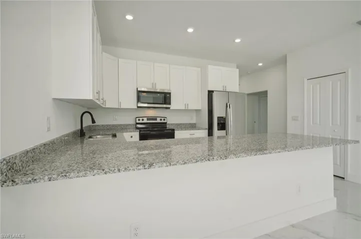 Kitchen featuring white cabinetry, stainless steel appliances, and light stone counters