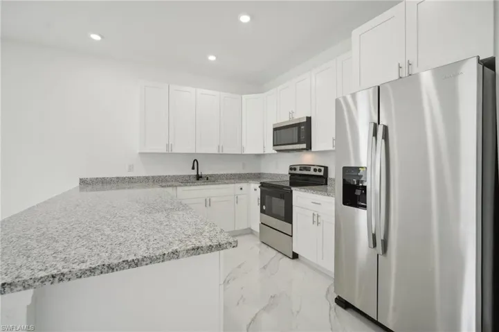 Kitchen with white cabinetry, light tile patterned floors, light stone counters, appliances with stainless steel finishes, and kitchen peninsula