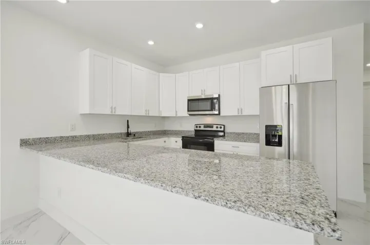 Kitchen featuring white cabinets, stainless steel appliances, light stone counters, and kitchen peninsula