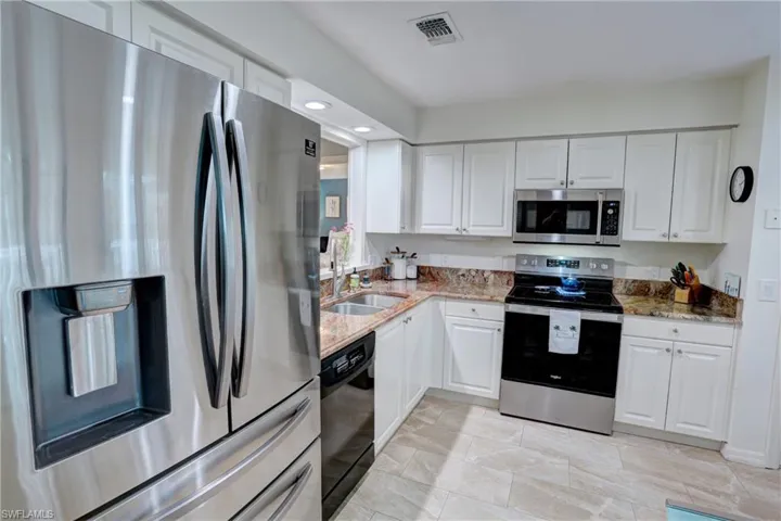 Kitchen featuring appliances with stainless steel finishes, white cabinetry, and light stone counters