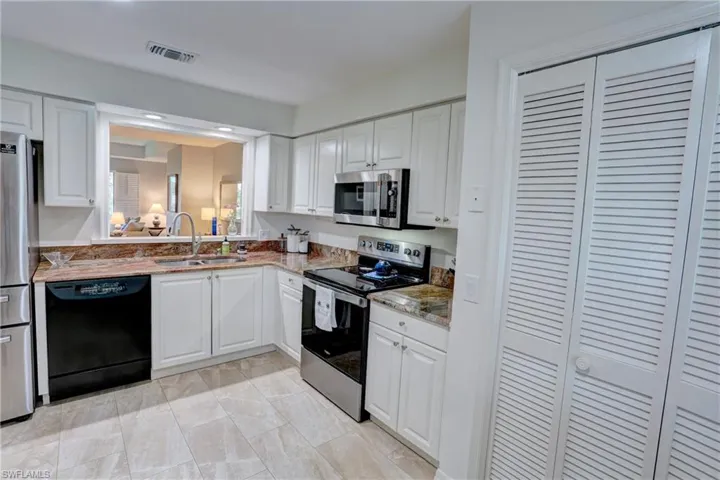 Kitchen with appliances with stainless steel finishes, sink, light stone countertops, light tile patterned flooring, and white cabinetry