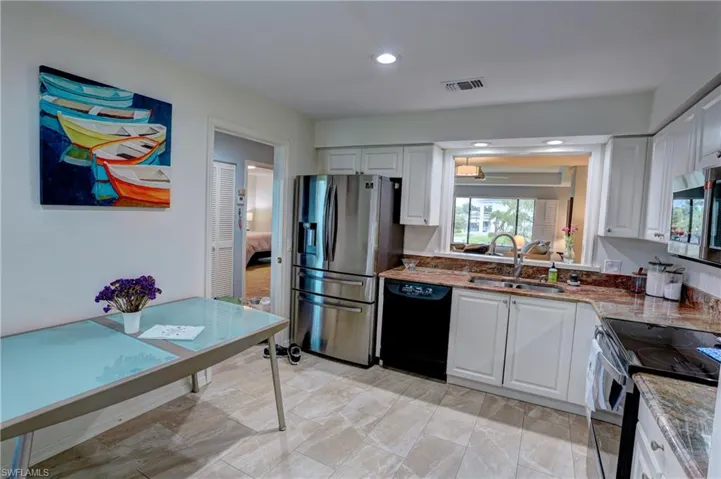 Kitchen with sink, light stone counters, stainless steel appliances, and white cabinetry