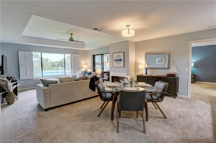 Carpeted dining room featuring a multi sided fireplace, ceiling fan, and a raised ceiling