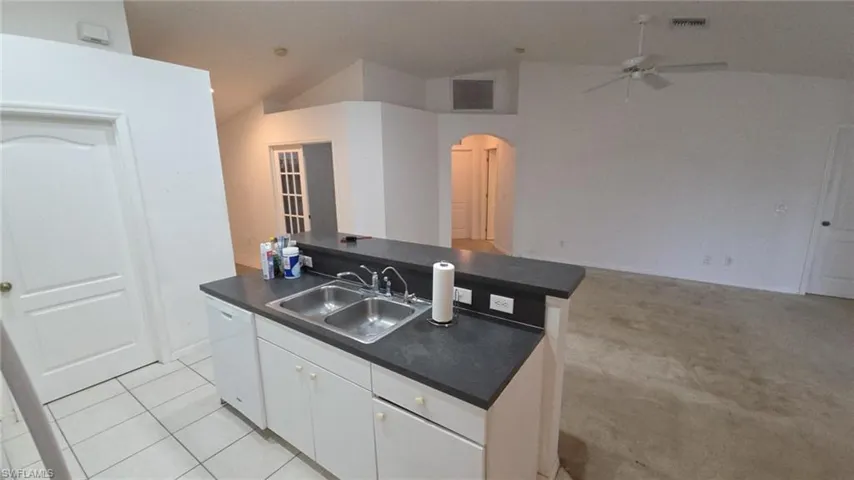 Kitchen featuring white cabinets, dark countertops, lofted ceiling, arched walkways, and an island with sink