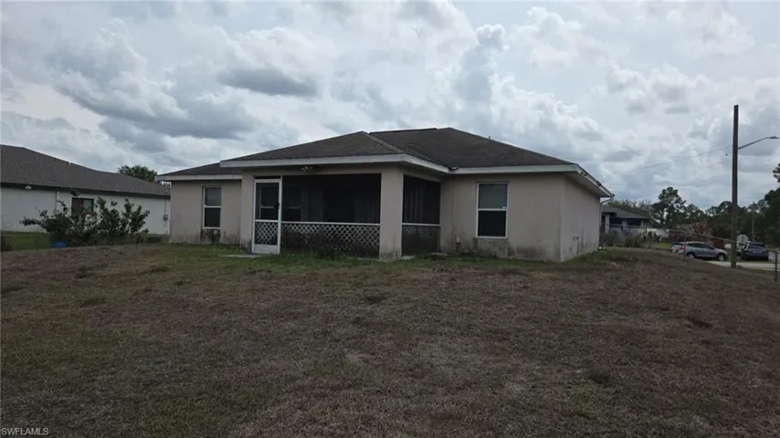 Back of property with a sunroom, stucco siding, roof with shingles, and a lawn