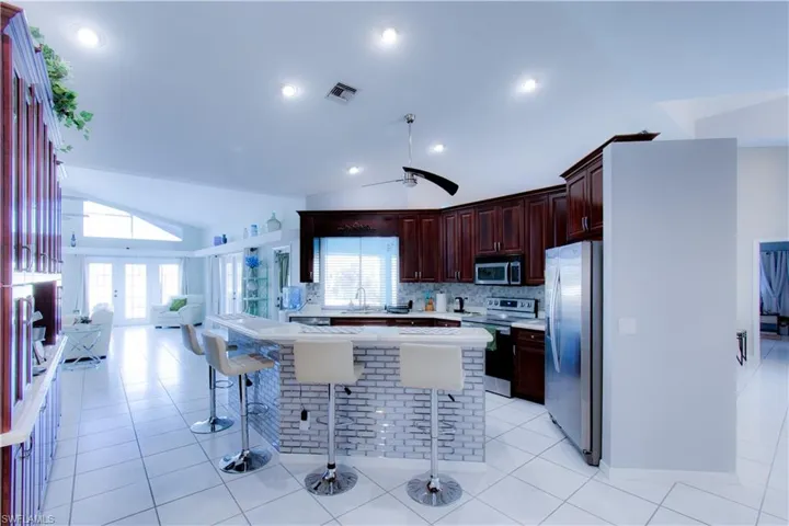 Kitchen featuring light countertops, lofted ceiling, stainless steel appliances, light tile patterned floors, and a kitchen bar