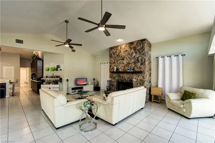 Living room with light tile patterned flooring, a fireplace, a ceiling fan, and high vaulted ceiling
