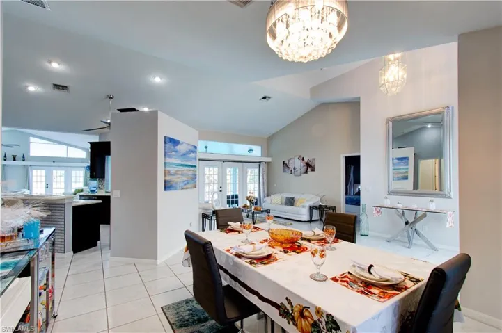 Dining area featuring french doors, light tile patterned floors, a chandelier, and high vaulted ceiling