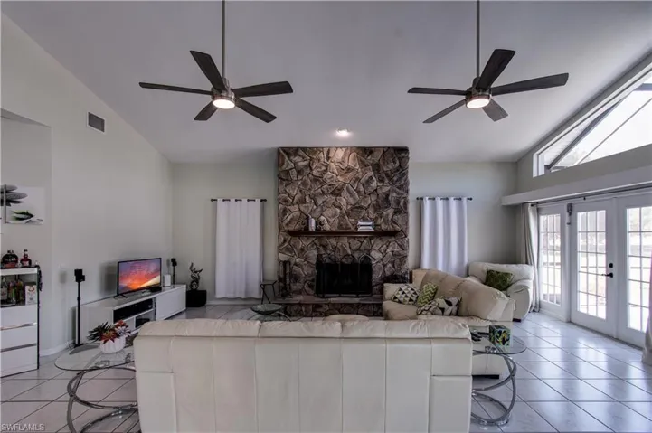 Living area featuring high vaulted ceiling, a fireplace, light tile patterned floors, ceiling fan, and french doors