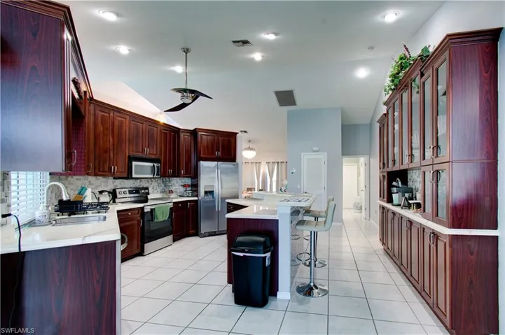 Kitchen with a kitchen bar, appliances with stainless steel finishes, vaulted ceiling, light tile patterned flooring, and a center island