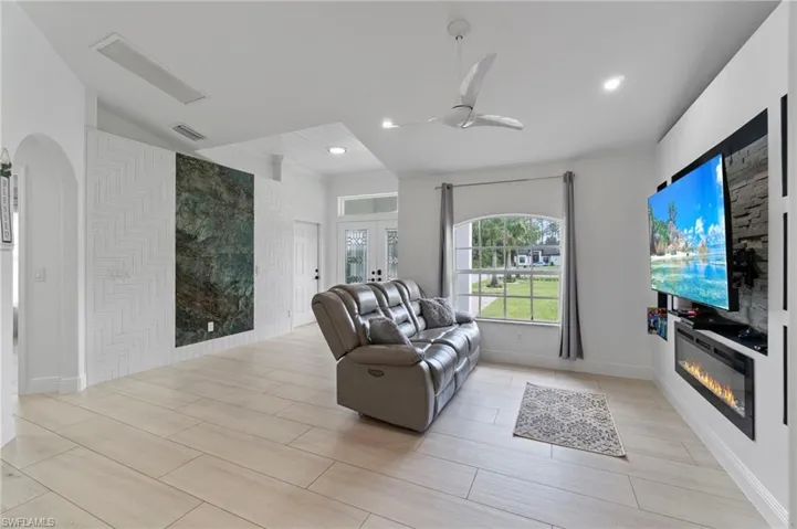 Living room featuring custom french doors, a glass covered fireplace, recessed lighting, and custom decorative wall.