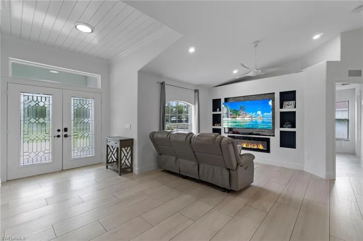 Living room with french doors, built in shelves, electric fireplace, recessed lighting, ornamental molding, and light wood-style floors
