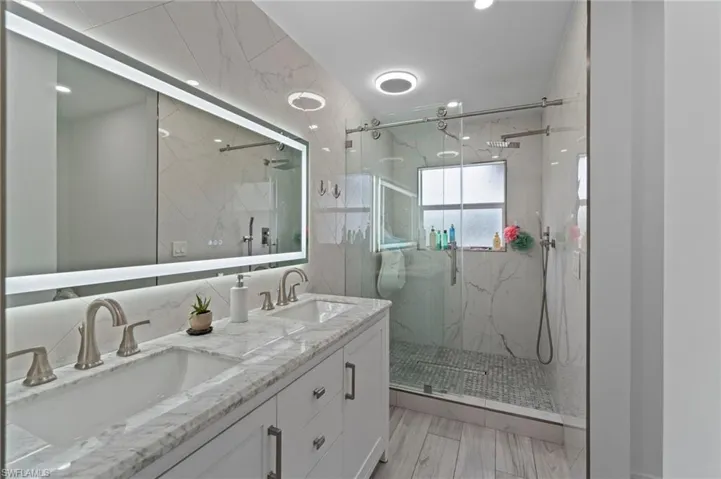 Bathroom featuring a marble finish shower, double vanity, and tile walls