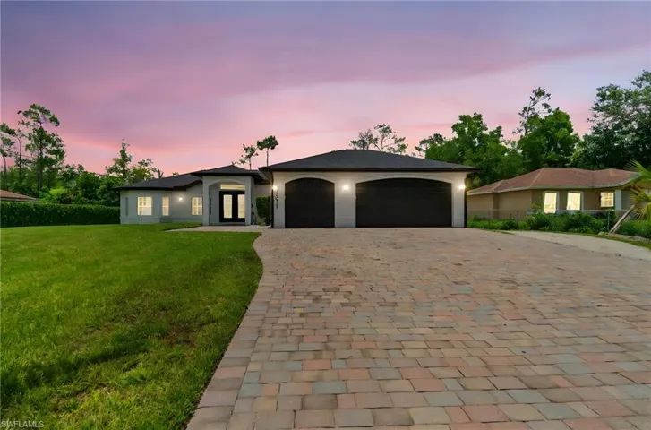 View of front of house featuring decorative driveway, a front yard, a garage, french doors, and stucco siding