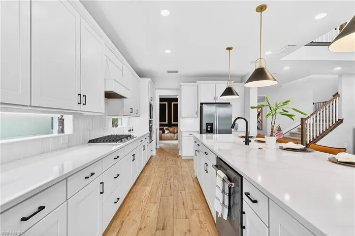 Kitchen featuring white cabinets, light wood finished floors, stainless steel appliances, tasteful backsplash, and decorative light fixtures