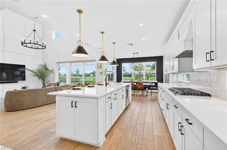 Kitchen with white cabinets, light wood-style floors, a kitchen island with sink, open floor plan, and light stone counters