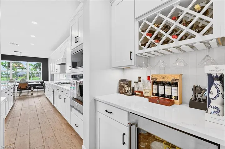 Kitchen with beverage cooler, white cabinets, light stone countertops, wood tiled floors, and stainless steel appliances