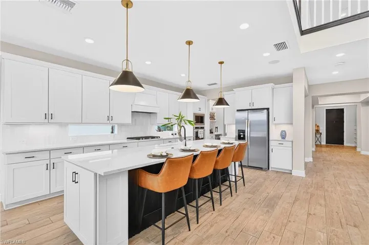 Kitchen with white cabinetry, stainless steel appliances, backsplash, light wood-style flooring, and decorative light fixtures