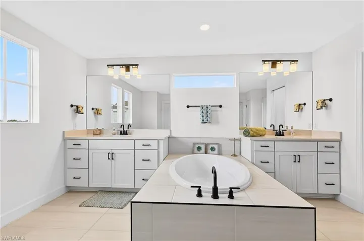 Full bath with a garden tub, two vanities, light tile patterned flooring, and recessed lighting