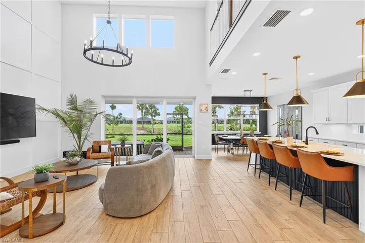 Living room with light wood finished floors, hanging lights, and a high ceiling