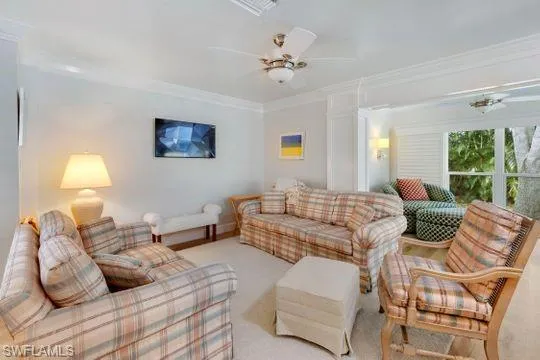 Living area featuring a ceiling fan, crown molding, and carpet flooring