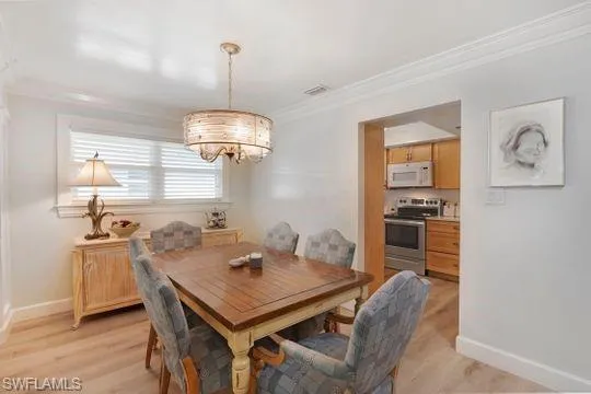 Dining space featuring crown molding, a chandelier, and light wood-style floors