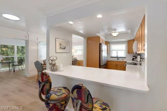 Kitchen featuring light countertops, light wood-type flooring, ornamental molding, freestanding refrigerator, and a breakfast bar