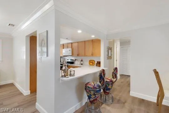 Kitchen featuring light wood-type flooring, light countertops, light brown cabinets, crown molding, and stainless steel range