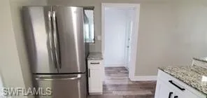 Kitchen with freestanding refrigerator, white cabinets, light stone countertops, and dark wood-type flooring