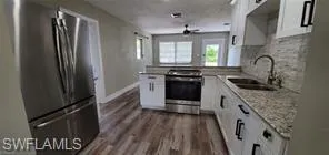 Kitchen with white cabinets, stainless steel appliances, dark wood-type flooring, a peninsula, and tasteful backsplash