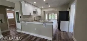 Kitchen featuring white cabinetry, a peninsula, a breakfast bar, dark wood-style flooring, and recessed lighting