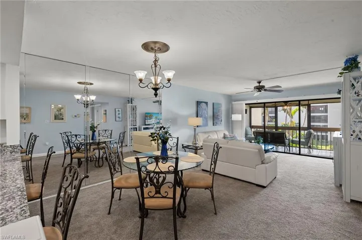 Carpeted dining space featuring ceiling fan with notable chandelier and a textured ceiling
