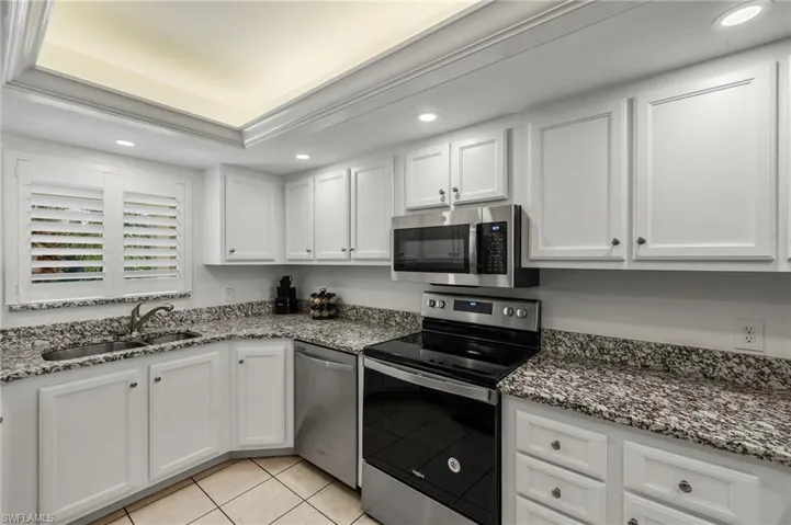 Kitchen with appliances with stainless steel finishes, sink, white cabinets, light tile patterned floors, and a tray ceiling