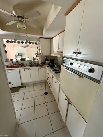 Kitchen featuring light tile patterned flooring, white cabinets, a tray ceiling, and white appliances