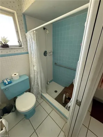 Bathroom with tile patterned floors, toilet, tile walls, and a shower with shower curtain
