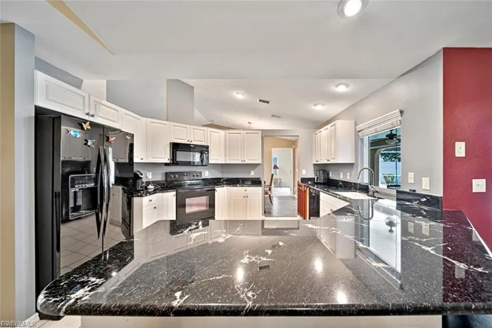 Kitchen featuring a peninsula, black appliances, lofted ceiling, white cabinets, and dark stone counters