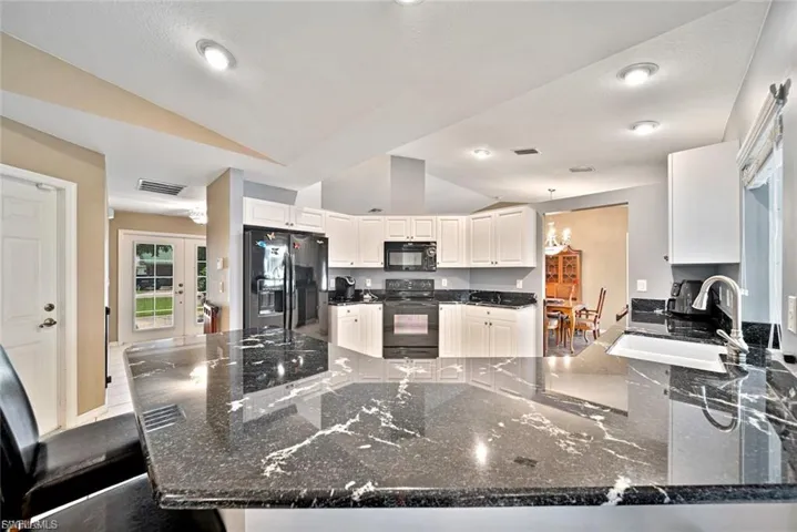Kitchen featuring a peninsula, dark stone countertops, vaulted ceiling, white cabinets, and black appliances