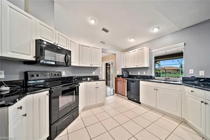 Kitchen with black appliances, white cabinets, dark stone counters, light tile patterned floors, and recessed lighting