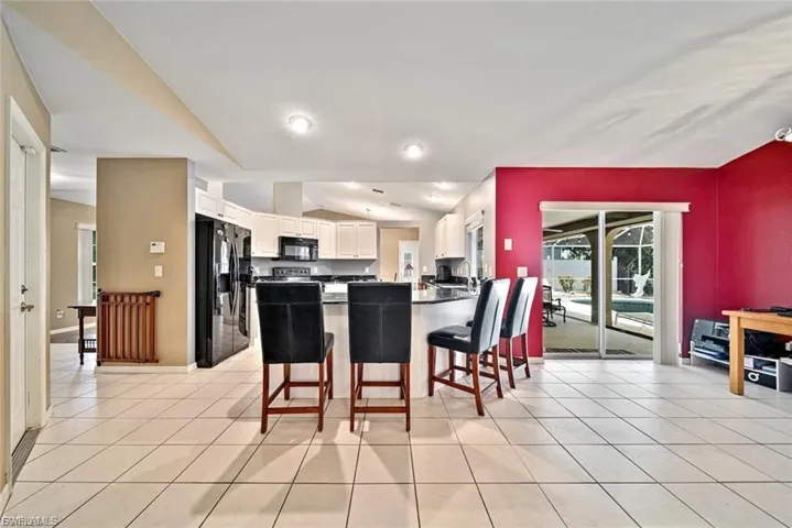 Kitchen with vaulted ceiling, black appliances, a breakfast bar area, white cabinetry, and a peninsula