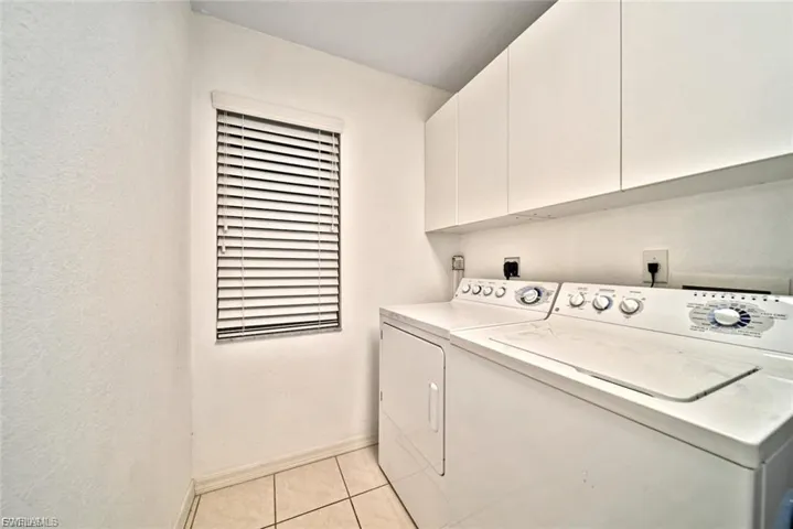 Washroom with washing machine and dryer, cabinet space, and light tile patterned flooring