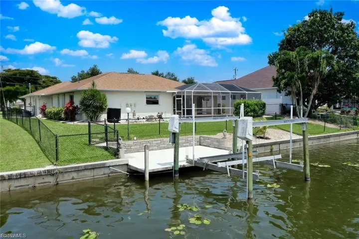 Dock area featuring a water view, a fenced backyard, a sunroom, boat lift, and a lanai