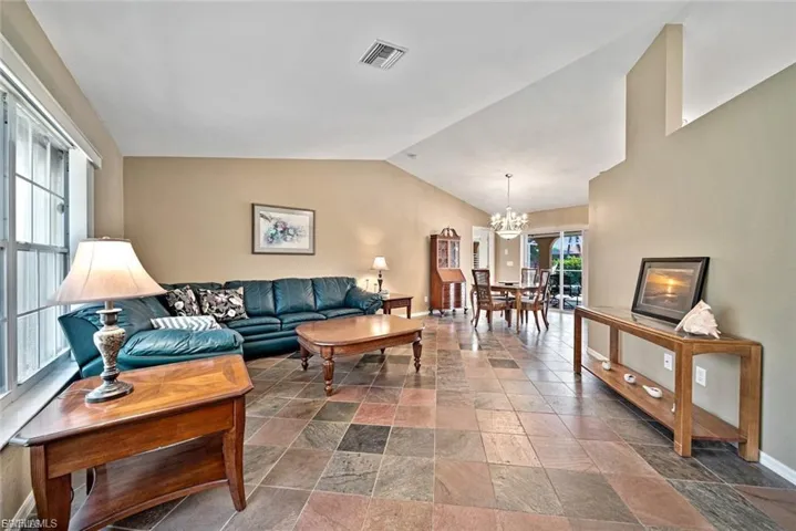Living room featuring lofted ceiling, a chandelier, and stone tile flooring