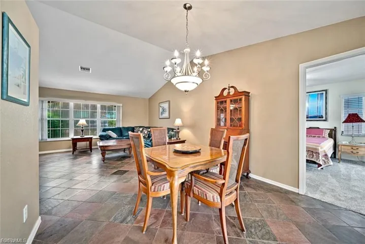 Dining area featuring vaulted ceiling, a chandelier, and stone tile floors