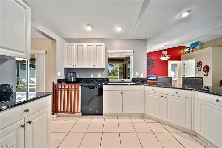 Kitchen featuring dark stone countertops, white cabinetry, black dishwasher, hanging light fixtures, and light tile patterned flooring